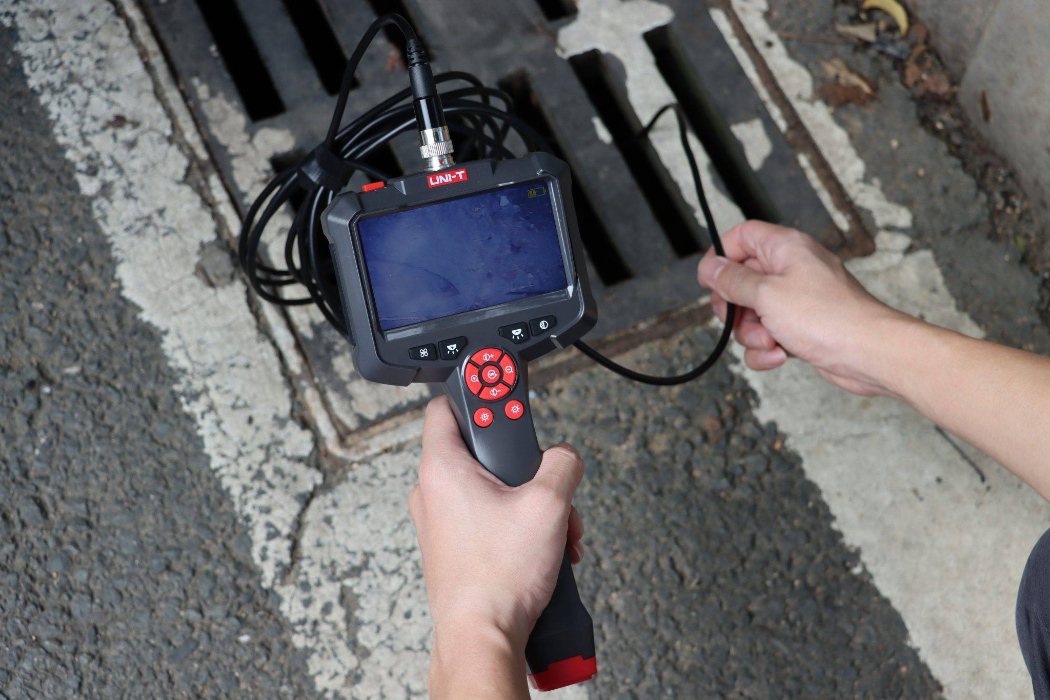 Ein Techniker führt die Sonde des UNI-T UT665P Endoskops in einen Abflussgitter ein.