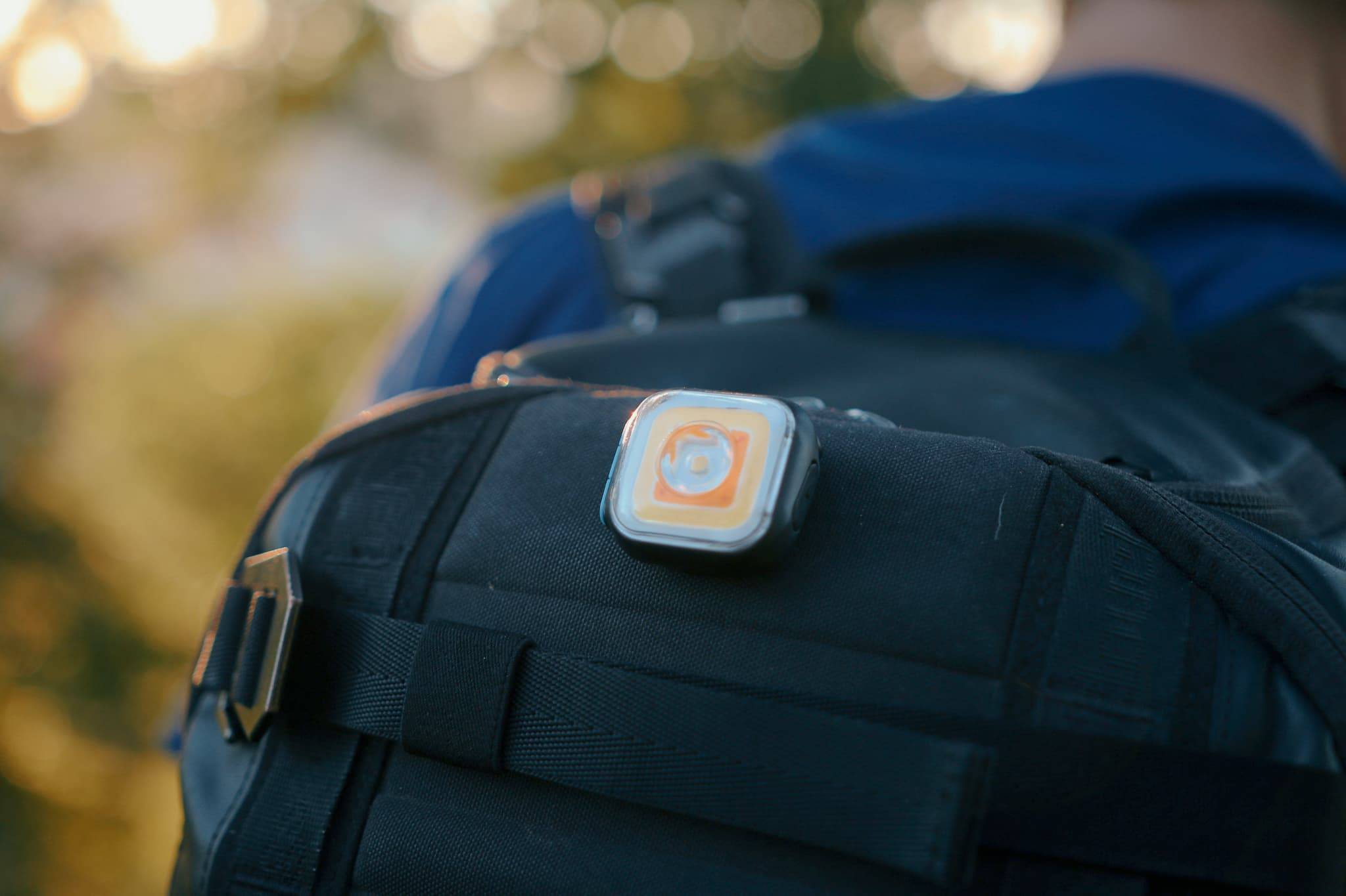 Nahaufnahme der MEOLINQ Light01 im Warmlichtmodus, befestigt an einem schwarzen Rucksack bei Sonnenuntergang.